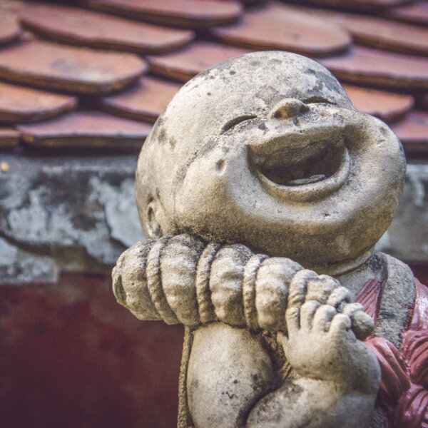 Lachender kleiner Buddha im Vordergrund eines Ziegeldachs